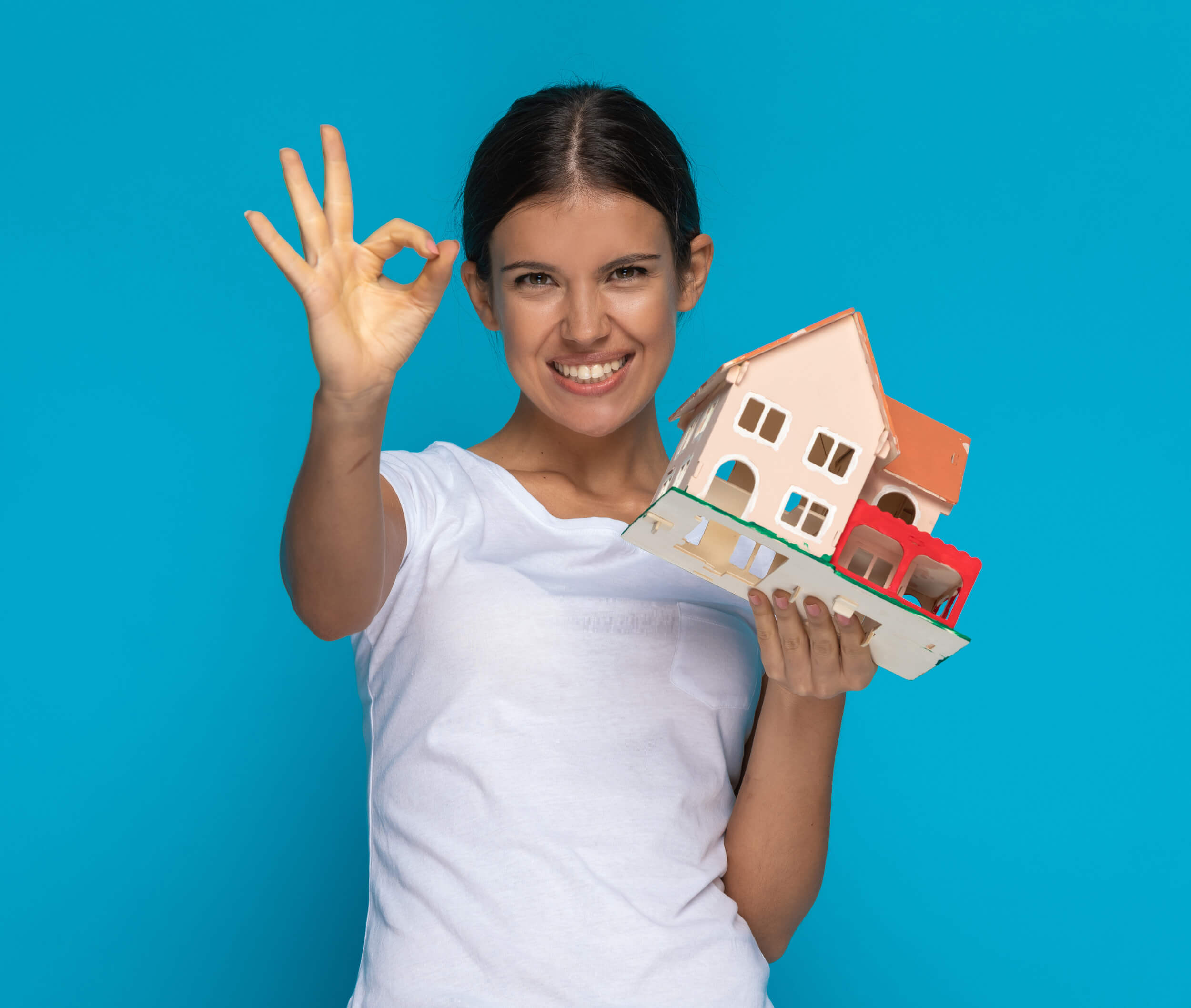 Femme tenant une petite maison dans la main et faisant un signe "ok"