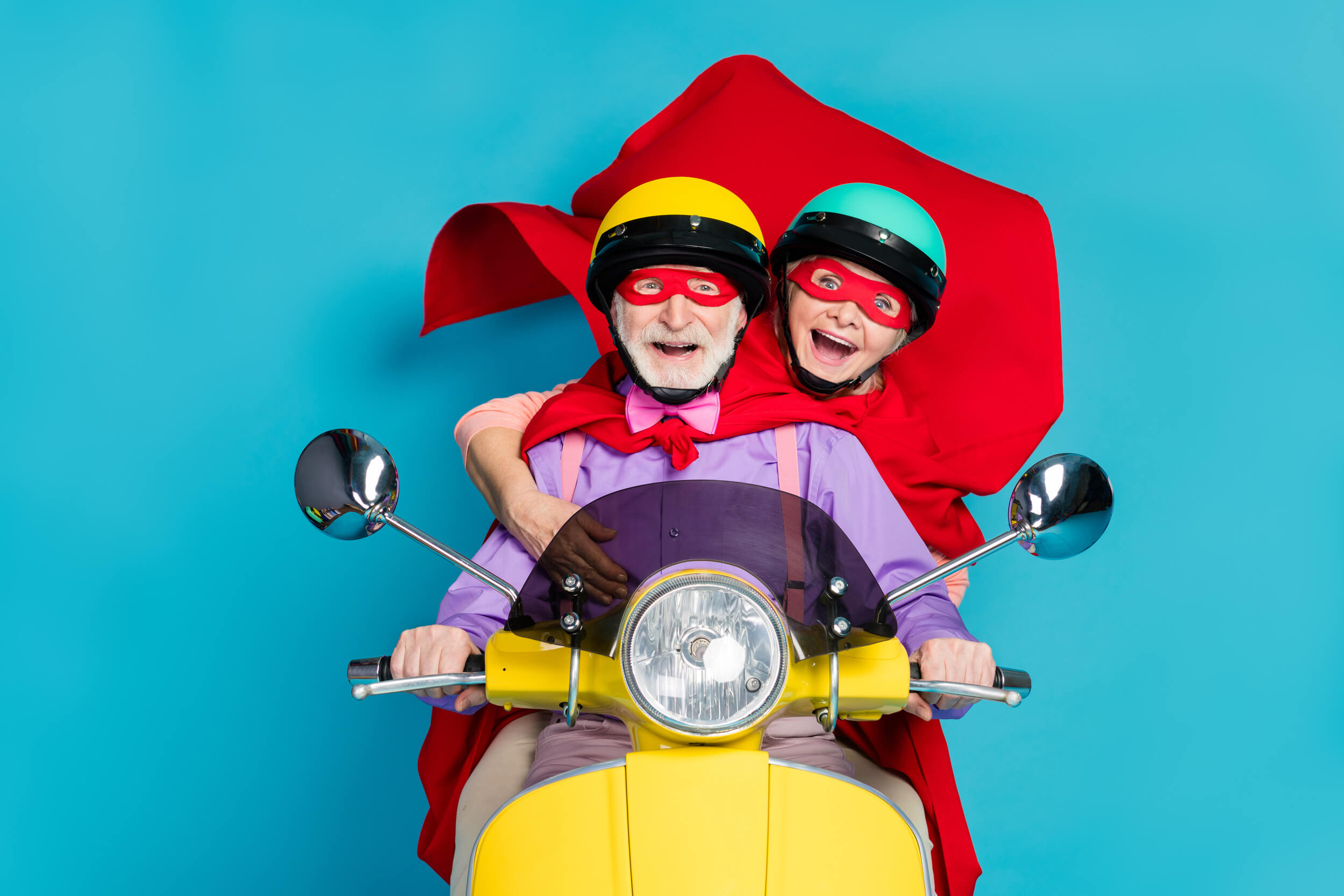 un couple de personnes âgées sur un scooter masqués et avec une cape